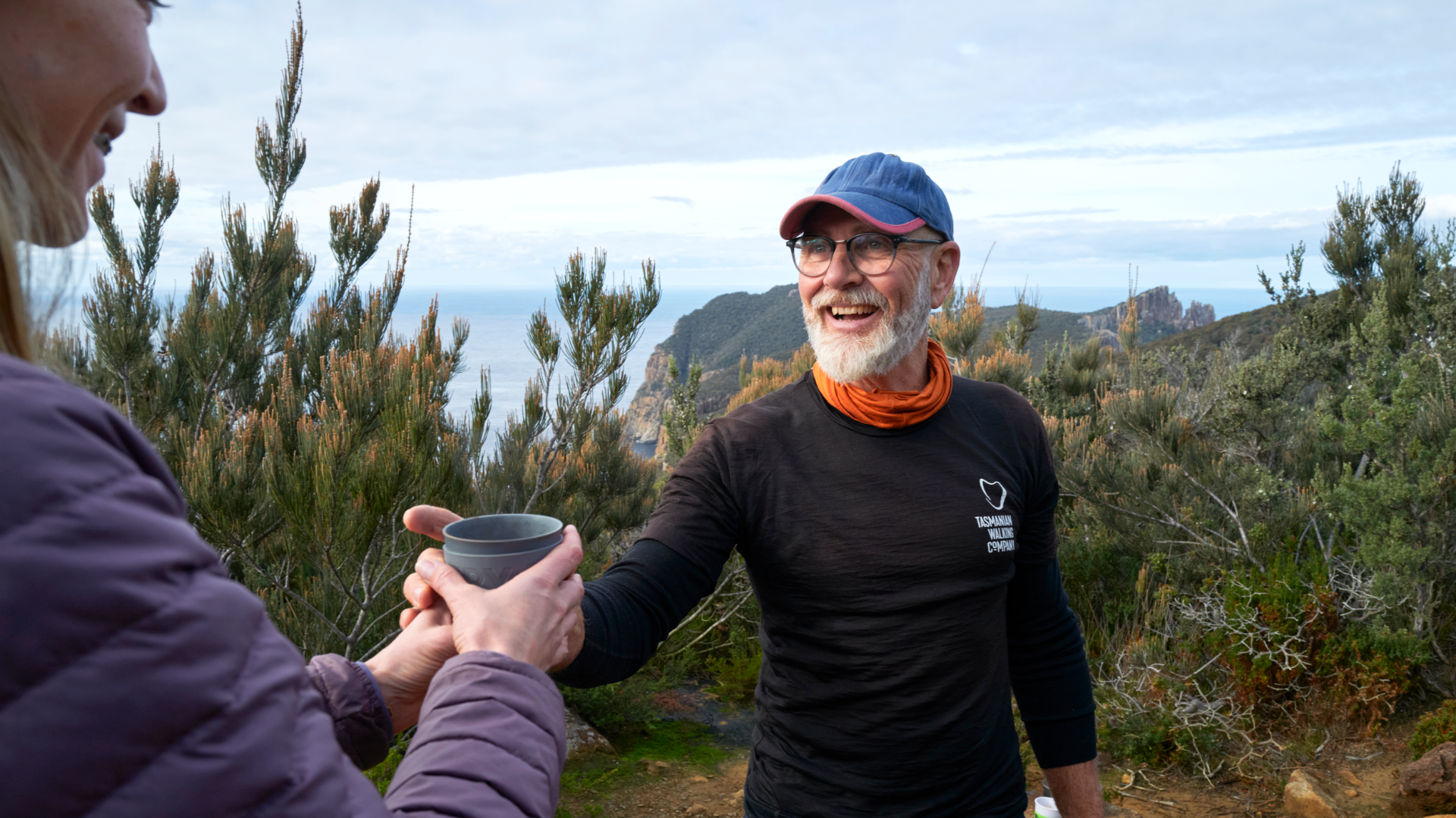 Person giving another person a cup of coffee in the wilderness