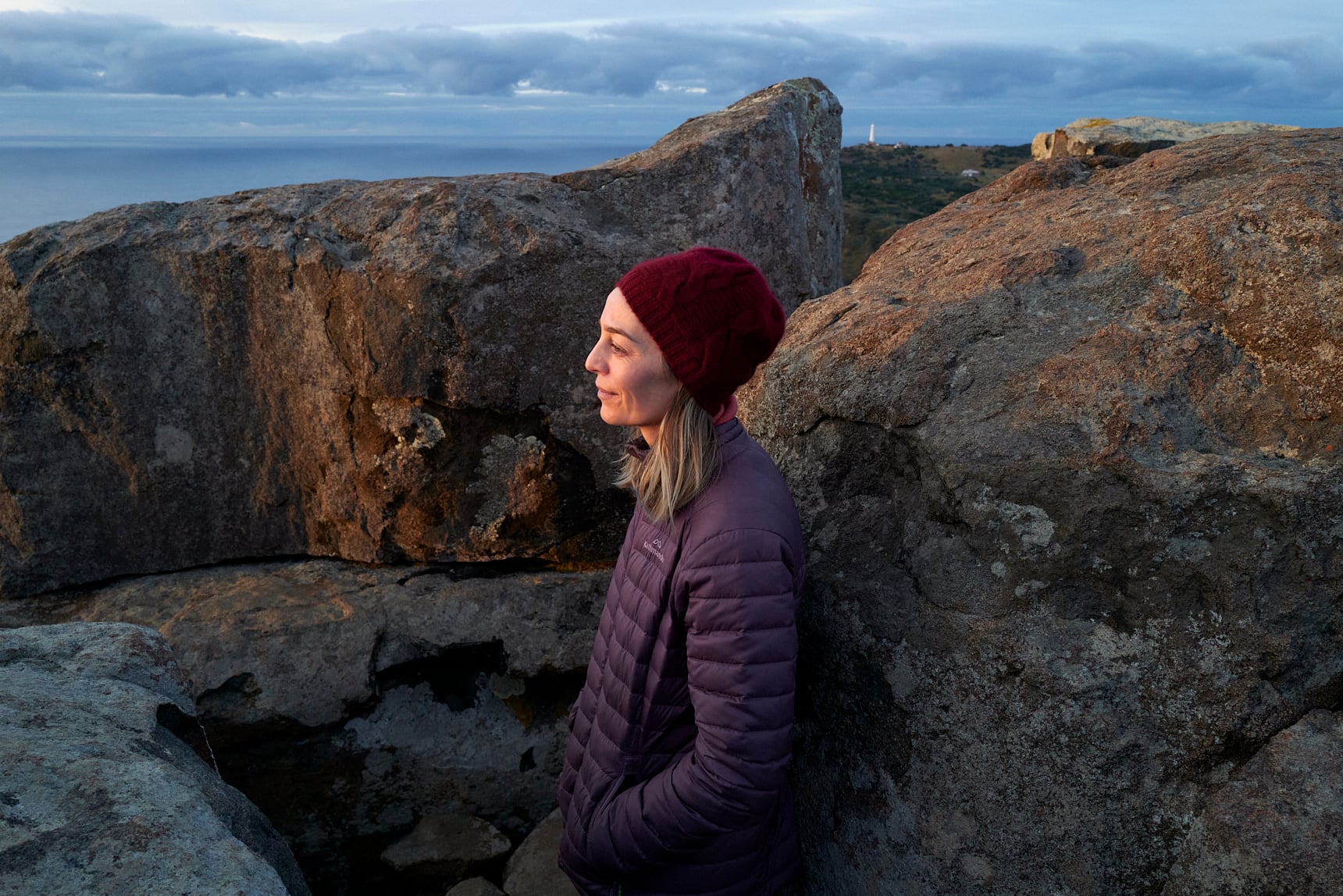 A person looking out at ocean at sunset from atop a mountain. 